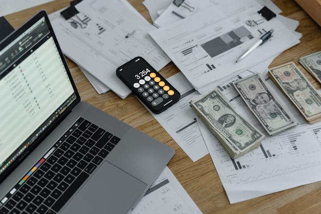 bank notes and a calculator alongside laptop and financial charts